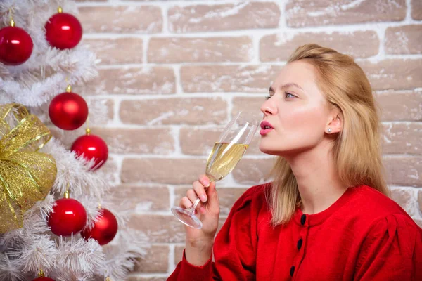 Женщина счастливо улыбаясь возле рождественской елки, наслаждается праздником. Сочельник. Концепция празднования Рождества. Ноэль и радость. Девушка в красном платье расслабляется с бокалом шампанского возле рождественской елки — стоковое фото
