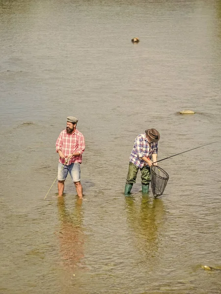 Haciendo juntos. actividad deportiva hobby. Cebo para truchas. dos pescador feliz con caña de pescar y red. recreación y ocio al aire libre. padre e hijo pescando. aventuras. Pesca de caza mayor. amistad masculina — Foto de Stock