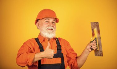 Sıva için alçı aletleri. sarı alçıpanlı alçıpanlı alçıpan spatulası. Üniformalı sıvacı, duvarları kapalı bir yerde sıva yapıyor. Spatulalı adam. Macun katmanının uygulanma süreci