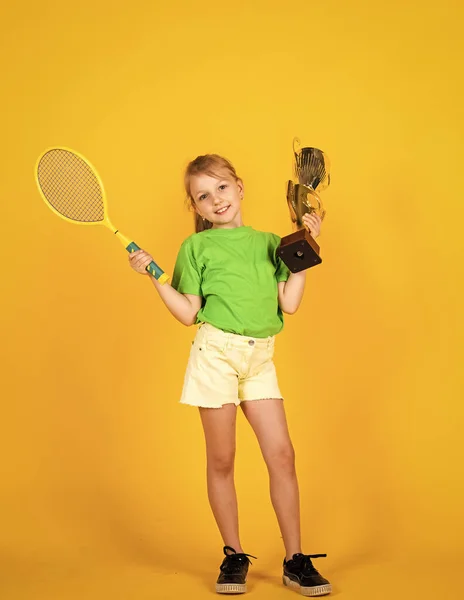 Lo sport è vita. piccola ragazza tenere coppa campionato e racchetta da tennis. Campione di badminton. Vittoria e vittoria. Risultati sportivi. concetto di successo sportivo. felice giorno dei bambini. infanzia felice — Foto Stock