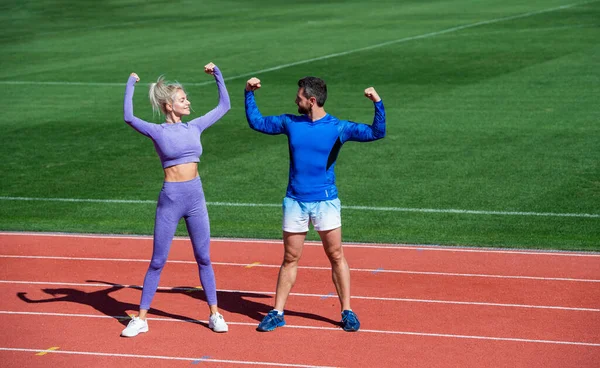 Fitness donna e uomo celebrano il successo o mostrano i muscoli bicipiti insieme sulla pista dello stadio all'aperto indossando abbigliamento sportivo, successo sportivo — Foto Stock