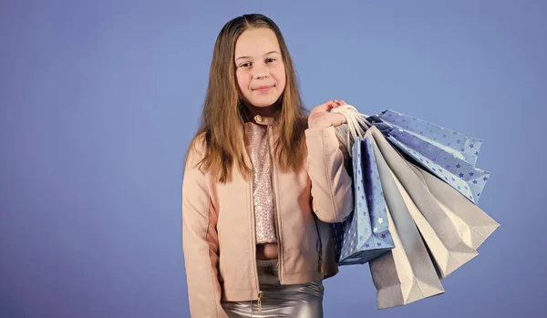 Ahorros en compras. Niños felices. Niña compras en línea sobre fondo azul. Ventas y descuentos. Moda infantil. asistente de tienda con paquete. Niña pequeña con bolsas de compras. espacio de copia —  Fotos de Stock