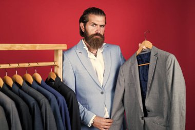 Askıdaki erkek kıyafetleri. Ceket arayan olgun bir adam. Askıda ceketi olan profesyonel bir erkek sartor. Mükemmel tasarım. Terzinin şık bir görünüşü var. Zarif takımlar sıraya dizilir