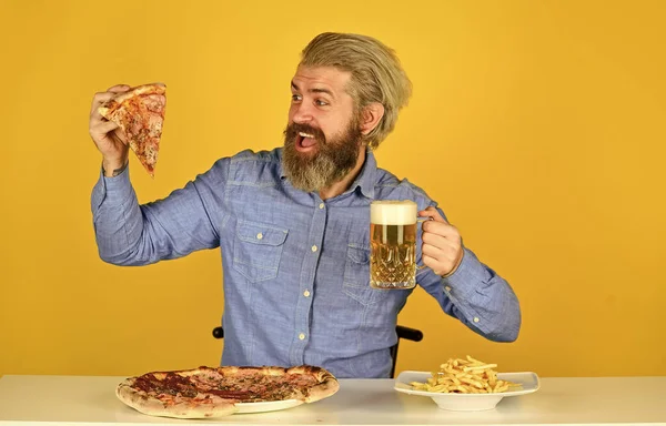 Frytki. Facet w barze pije piwo i je pizzę. Zdrówko. oglądanie futbolu w telewizji. Amerykańskie fast foody. szczęśliwy brodaty mężczyzna z pizzą i piwem. włoska żywność — Zdjęcie stockowe