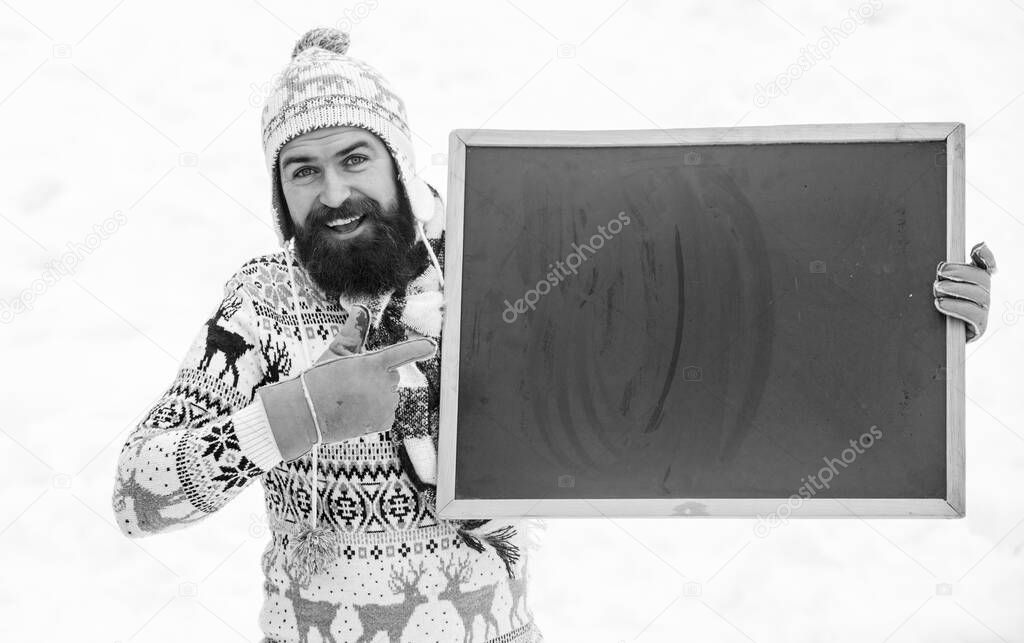 point finger. winter season. Christmas sales. happy hipster with blackboard. man advertising board. Copy space. winter holiday. Party here. bearded man in warm clothes. Happy new year. ski and sledge