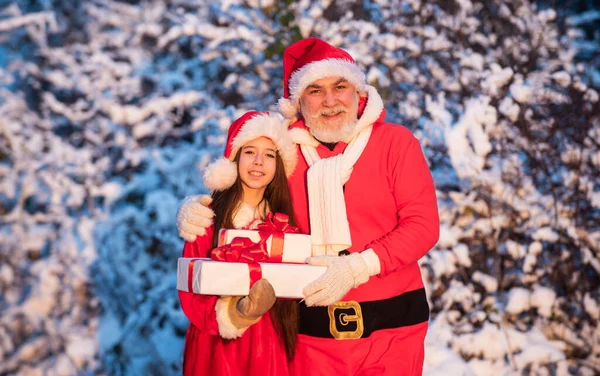 Was für eine große Überraschung. Opa im Weihnachtsmannkostüm mit kleinem Mädchen. Weihnachtsmann-Helfer mit Geschenken im Freien. schönen schneebedeckten Winter. Kind und Senior bereit zum Feiern. Winterurlaub und Urlaub — Stockfoto