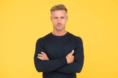 Yakışıklı, kendine güvenen bir adam ellerini çapraz yapmış şık bir saç şekli ve sarı arka planda tüylü bir yüzü var.