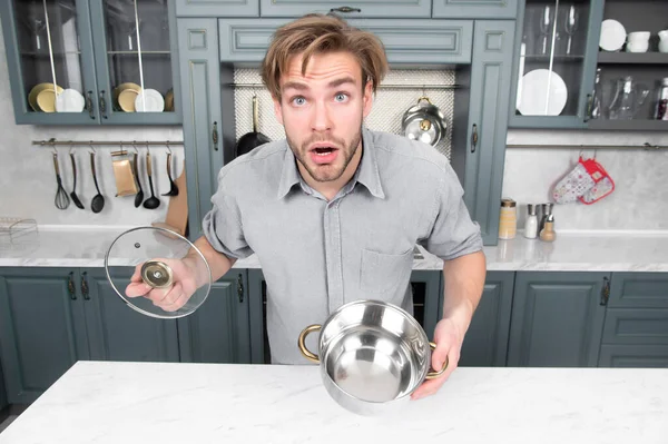 Хлопець з здивованим обличчям тримає відкриту каструлю, кришку на кухні — стокове фото