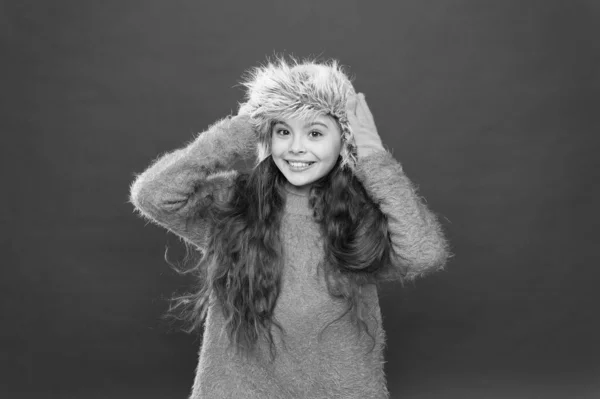 Pequeño concepto fashionista. Me siento tan cómodo. Niño sombrero de pelo largo suave. Concepto de moda de invierno. Sombrero cálido para clima frío de invierno. Niña sonrisa fondo rojo. Accesorio peludo suave. Temporada de invierno — Foto de Stock