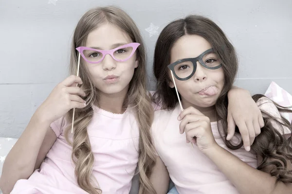 Playful mood. Girls children posing with grimaces photo booth props. Pajamas party concept. Girls friends having fun pajamas party. Friends cute and cheerful posing with eyeglasses accessories — Stock Photo, Image