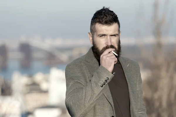 Smoking devices concept. Bearded hipster smoking outdoors. Device hide conceal smell of smoke. Handsome man smoke flying out of mouth. Cigarette tobacco harmful health influence. Smoking aesthetics