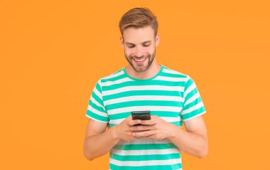 SMS mesajı gönderiliyor. Mutlu adam SMS 'i akıllı telefon sarı arka planıyla gönderiyor. SMS mesajı. Kısa mesaj servisi. Yeni teknoloji. Taşınabilir yaşam tarzı. Modern hayat. Güvenilir SMS teslimatı