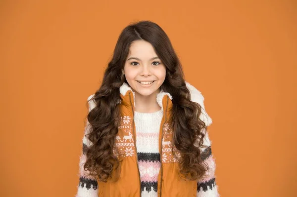 Fröhliches Teenie-Mädchen mit langen lockigen Haaren trägt Puffweste und Pullover mit weihnachtlichem Muster, Winterkleidung — Stockfoto