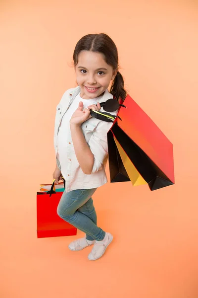 Happy gyermek tartsa bevásárló táskák sárga háttér. Egy kis bolti mosoly papírzacskókkal. Lány vásárló készülj a születésnapra, divat. Fekete Péntek koncepció. Jó szórakozást a vásárláshoz. Nagy üzlet. — Stock Fotó