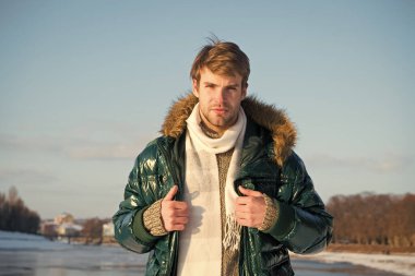 Fotoğraf için poz veriyorum. Yakışıklı, yeşil kabarık ceketli adam. Adam güneşli kış gününün tadını çıkarıyor. Erkek sezonluk moda. Soğuk algınlığı ve grip Kürk kapüşonlu erkek. Sıcak ve rahat hissediyorum. favori sezon
