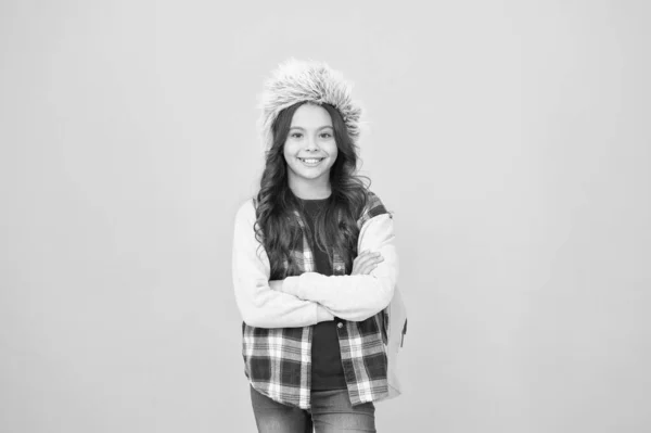 Το μικρό κορίτσι φοράει καπέλο από πτερύγιο. χειμερινό σχολείο και διακοπές. χειμερινά μαθήματα εκπαίδευσης. σχολική τσάντα κίτρινο φόντο. περίοδος επιλογής μαθημάτων. ανέμελος μαθητής παιδί. Προς τη γνώση — Φωτογραφία Αρχείου