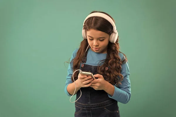 Contesta el correo electrónico. niño pequeño hacer lista de juegos en el teléfono inteligente. niña pequeña utilizar reproductor de mp3. estudiar en la vida moderna. chica utilizar dispositivo digital. moda casual para niños. cabellos largos escuchar música en los auriculares — Foto de Stock