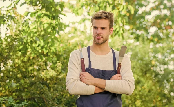 Picknickkonzept. Bbq Koch. Sommerwochenende. Werkzeuge zum Braten von Fleisch im Freien. Grillparty. Schöner Typ, der Essen kocht. Grillen. Grillutensilien. Burger kochen. Mann hält Grillgerät in der Hand — Stockfoto