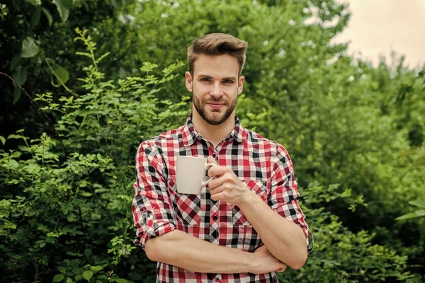 good morning. fresh inspiration and energetic beverage. handsome bearded guy drinking tea outdoor. he loves cocoa. food and drink. cheerful man in checkered shirt drink morning coffee
