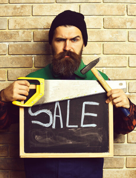 bearded foreman holding various building tools with serious face