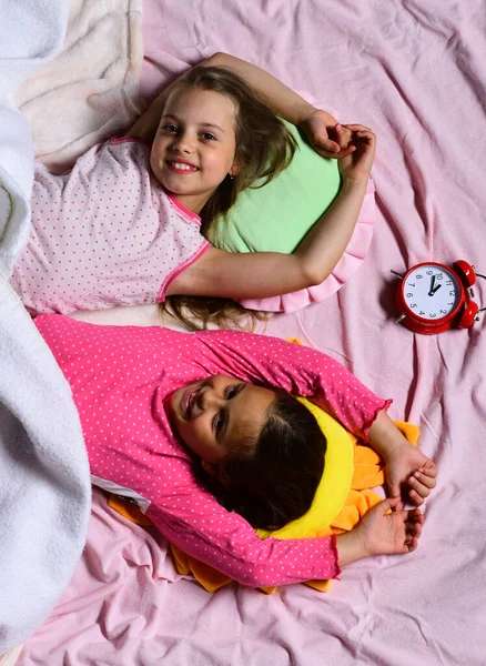 Schoolgirls in pink pajamas wallow on colorful pillows, top view — Stock Photo, Image