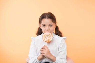 Yetersiz beslenme yaygın bir sorundur. Kız öğrenci üniforması lolipop şeker sarısı arka plandan hoşlanıyor. Şirin kız at kuyruklu, saç stili tatlı lolipop yiyor. Uygun oranlarda şekerleme. Tamam.