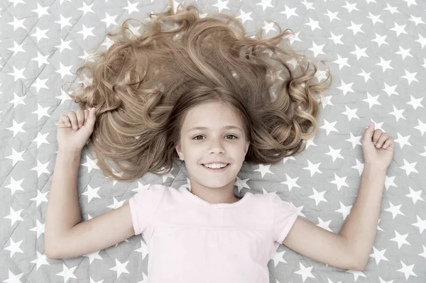 天然カールは治療とケア。長い巻き毛の女の子の子供はベッドの上のビューに横たわっていた。子供の完璧な巻き毛はかわいいように見えます。コンディショナーマスク有機オイルは髪の光沢のある健康を維持します。すごいカールのヒント — ストック写真