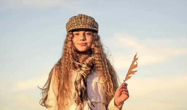 Наслаждаюсь осенним днем. стильная маленькая девочка в осеннем бере. Осенние тенденции. Детская мода. Небо погоды. Счастливого детства. Концепция парикмахерской. Маленькая девочка с вьющимися волосами. ребенок держит осенний лист