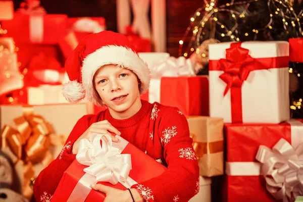 Заінтригований милий Санта. Маленький щасливий хлопчик знаходить подарунки біля ялинки. Магазин подарунків. Дитячі різдвяні подарункові коробки з капелюхом Санта. Веселого Різдва. Краса зими. Дозвілля та активність. День боксу — стокове фото