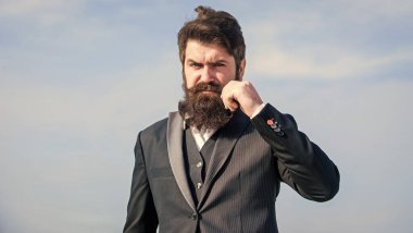 Sakallı hippi adam resmi takım elbise giyer mavi gökyüzü arka planı. Klasik sakal. Sakal ve bıyık bakımı. Sakal modası modası. Tımar rutiniyle başla ve daha iyi bir dünya kur.