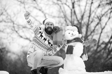 Noel öncesi. Kış tatili Soğuk havada sıcak kazak. Mutlu hipster Noel 'e hazır. Sakallı adam kardan adam yapar. Mutlu yıllar. Kış mevsimi. Mutlu noeller. Noel Baba hediyesini dışarıda verir.