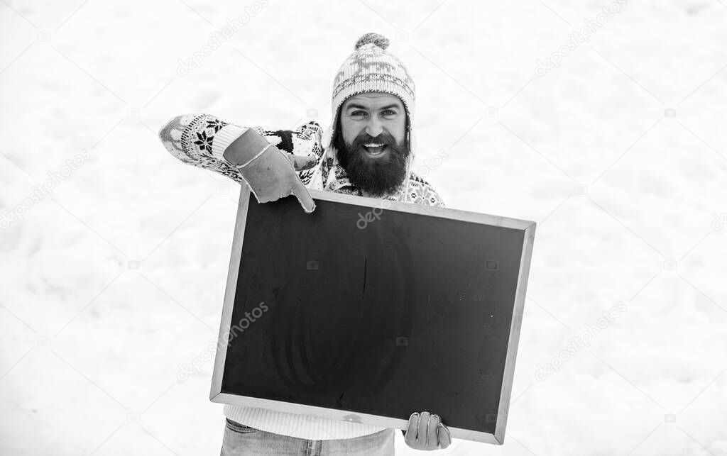 look here. bearded man in warm clothes. Happy new year. happy hipster with blackboard. man advertising board. Copy space. winter season. ski and sledge. Christmas sales. winter holiday. Party here