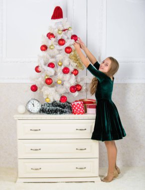 Kids can brighten up christmas tree by creating their own ornaments. Girl celebrate christmas. Top christmas decorating ideas for kids room. Child hang christmas ornament ball on artificial tree clipart