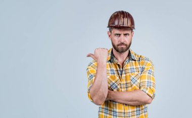 İnşaat kaskı ve inşaat sahasında kareli gömlek giyen yakışıklı bir işçi. Finegr 'i işaret ediyor. Kopya alanı, reklam.