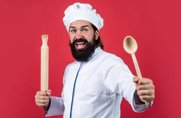 Хипстер шеф-повар в шляпе с бородой и усами на красном фоне использовать деревянные кухонные принадлежности, приготовление пищи — стоковое фото