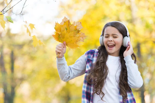 トレンディな美しさ。子供の頃の幸せ。美しさと自然。幸せな子供はヘッドフォンを着用する。10代の女の子は学校に行く途中で音楽を聴く。子供は秋の森を歩く。公園にもみじの葉が落ちる。オンライン教育 — ストック写真