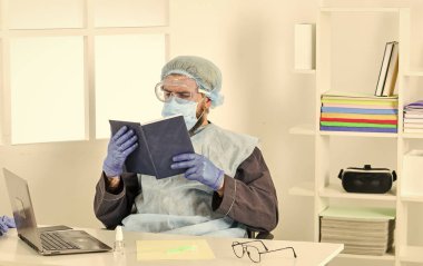 Kendini nasıl koruyacağını öğren. Adam kitap okuyor. Tıbbi araştırma. Koruyucu ekipman işçisi. Doktor çalışıyor. Coronavirüs salgını. En son bilimsel bulgular ve koronavirüs hastalığı hakkında bilgi