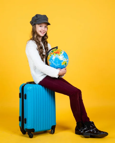 Vrolijk kind in hoofddeksel met valise voor reizen op gele achtergrond, vakantie — Stockfoto