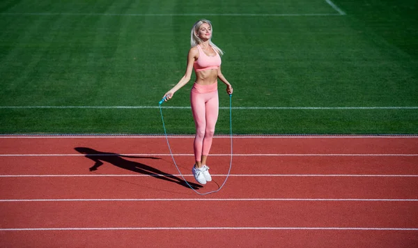 sexy lady in fitness sportswear. jumping on outdoor arena. training and workout. athletic female coach with skipping rope. woman sport trainer. healthy sporty lifestyle. health and energy