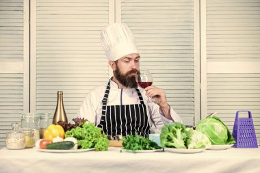 Adam şapka takar ve önlük giyer. Usta şef bir bardak şarap tutuyor. Biraz alkol ekle. Yemekte hangi şarap servis ediyor? Şarap arıtma. Mutfak konsepti. Şarap ve yemekleri uzman gibi eşleştir.