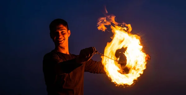 Happy guy artist perform fire ring by spinning burning poi on idyllic dark sky at night outdoors, circle