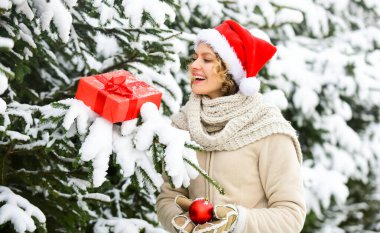 Hey, hey. Kış alışveriş mutluluğu. Açık hava mükemmel bir ruh halidir. Satış ve indirim. Mutlu kadının elinde Noel hediyesi kutusu var. Noel ağacı süslemeli kız. Bayan Kırmızı Noel Baba şapkası kürk ağacında