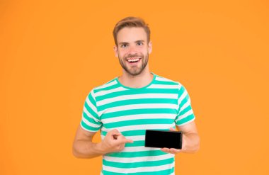 Senin için en iyi telefon. Akıllı telefonun sarı arka planına bakan mutlu adam. Reklam için işaret. İşaret parmağı. Gösterişli bir jest. En iyi seçim. Bu aslında hayatını kolaylaştıracak.