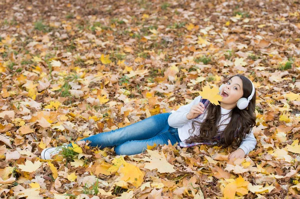 Őszi gyerek divat. inspiráció. Boldog gyermekkort. Vissza az iskolába. lány juharfalevelek között pihenjen a parkban. őszi szépség az erdőben. Élvezze a zenét a fülhallgatóban. online oktatás és e-tanulás. Őszi öröm — Stock Fotó