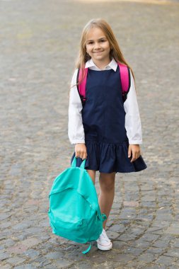 Moda üniformalı küçük mutlu çocuk dışarıda sırt çantası tutuyor, okula geri dönüyor.