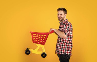 Küçük alışveriş arabalı komik adam. Haftasonu ürünler alıyoruz. Başarılı alışverişler yapıyor. Akılsızca para harcıyor. Müşteri arabası. Süpermarkette alıcı. Boş oyuncak vagonu. Adam alışverişe gidiyor.