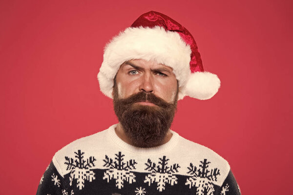 serious bearded man santa hat. brutal hipster favorite sweater red background. winter holiday fun. serious face mustache. portrait of santa man with beard. new year party. christmas eve