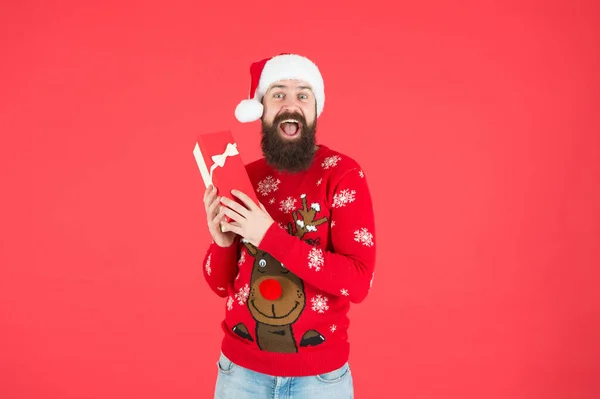 Счастливый бородатый мужчина хипстер носить смешной вязаный свитер и Санта-Клаус шляпу и держать подарок коробка есть идея для празднования рождественской вечеринки, рождественские покупки — стоковое фото