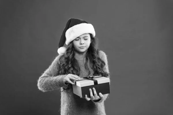 secret present. small girl in santa hat. cheerful child red wall. kid shopping sales. xmas boxing day. best christmas offer. little girl hold present box. happy new year gift. christmas holiday party