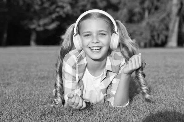 Foi um belo dia. relaxar na grama verde em fones de ouvido. menina pequena ouvir áudio livro. nova tecnologia para crianças. memórias felizes da infância. ouvir música. de volta à escola. Kid estudo no parque — Fotografia de Stock